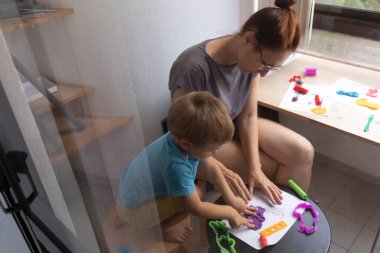 Anne ve oğlu yaratıcı oyun zamanlarını seviyorlar, evdeki renkli killeri kağıt üzerinde şekillendiriyorlar.