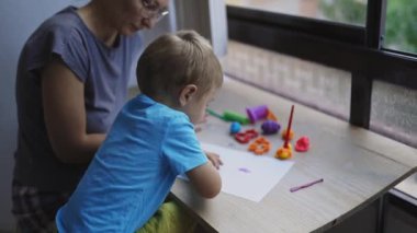 Anne oğluna pencerenin yanında renkli kil sanatı yapmayı öğretiyor.