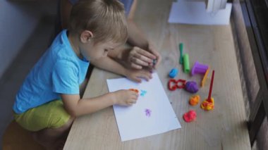 Anne, oğlunun kille renkli sanat eserleri yapmasına yardım ediyor.