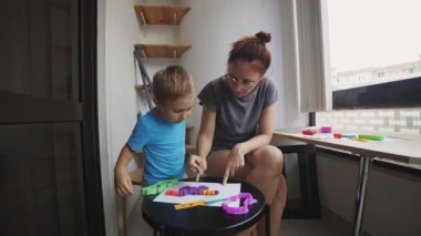 Anne, evinde renkli oyuncaklar kullanarak oğluna temel matematik ve sayıları öğretiyor.