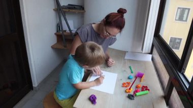 Anne, oğlunun pencere kenarındaki bir masada kille sanat yaratmasına yardım ediyor.