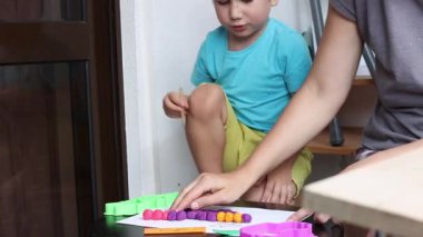 Genç bir çocuk, annesinin rehberliğinde kilden modellik yaparak öğreniyor ve eğleniyor.