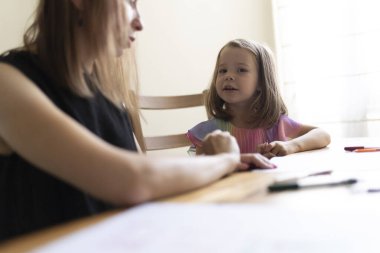 Anne, küçük kızına ödevlerinde yardım ediyor, pozitif bir öğrenim ortamı sağlıyor.
