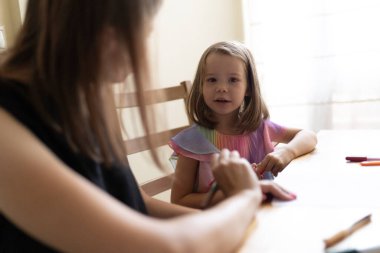 Bebek bakıcısı evde renkli kalemlerle çizim yapan küçük bir kıza yardım ediyor, yaratıcılığı ve öğrenmeyi oyun yoluyla teşvik ediyor.