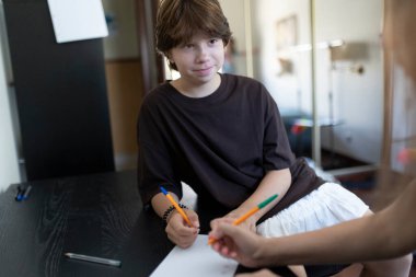 Bir kağıda yazı yazan bir çocuk ve özel öğretmeni evde ona yardım ediyor.