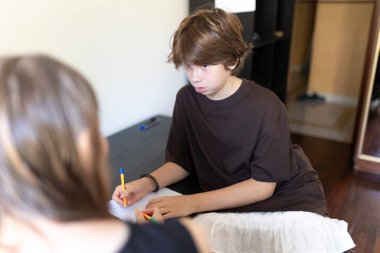 Genç bir çocuk öğretmeniyle evde eğitim seansı sırasında renkli kalemlerle resim çizerken konsantre oluyor.