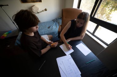 Öğretmen genç bir öğrenciye ev ortamında okul egzersizlerinde yardım ediyor.