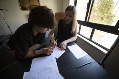 Genç bir öğrenciye okul ödevlerinde yardım eden, evde öğrenim ortamında rehberlik ve destek veren bir bayan öğretmen.