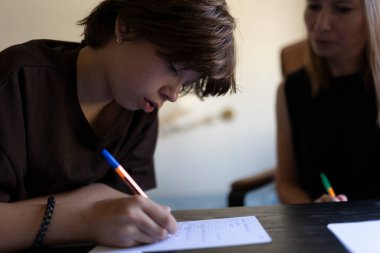 Bayan öğretmenle özel ders sırasında not defterine notlar yazan odaklanmış ergen öğrenci.