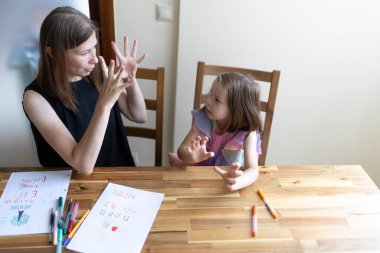 Öğretmen, bir evde eğitim sırasında parmak ve çizimler kullanarak genç öğrencilere numara öğrenmede yardım ediyor.