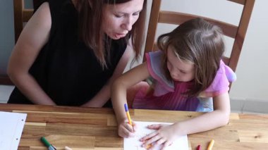 Anne küçük kızına renkli kalemlerle resim yapmayı öğretiyor.