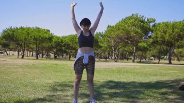 Spor hocası parkta esneme hareketleri yapıyor.