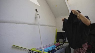 Beyaz bir tavan arasında çamaşır asan bir ev hanımı.