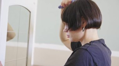 Bir insan aynaya bakarken kısa saçlarını tarıyor.