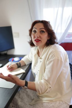 İş kadını ofiste konuşurken not alıp el kol hareketi yapıyor.