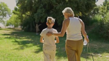 Anne ve oğlu parkta yürüyorlar ve başka bir çocuğu uzaktan izliyorlar.