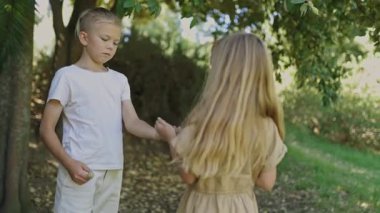 Genç bir kız ve oğlan nesneleri değiş tokuş ediyor ve güneş ışığıyla dolu yemyeşil bir park ortamında sıcak bir etkileşim içindeler.