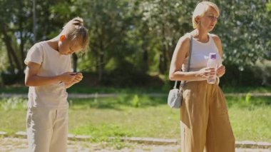 Annesi elinde tekrar kullanılabilir bir su şişesi tutarken genç bir kız sopayla oynuyor.