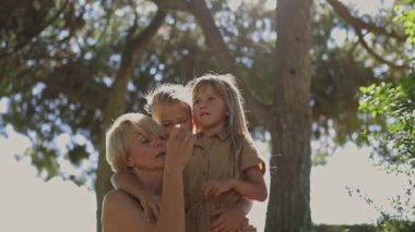 Anne parkta iki çocuğuna sarılıp oynuyor.