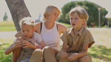 Anne ve çocuklar parkta bir ağacın altında oturmuş sohbet ediyorlar.