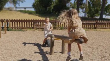 İki çocuk oyun parkında tahterevalli sürüşünden zevk alır.