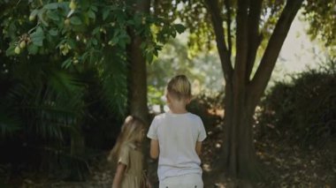 Ağaçlar ve çalılarla parkta saklambaç oynayan iki çocuk.