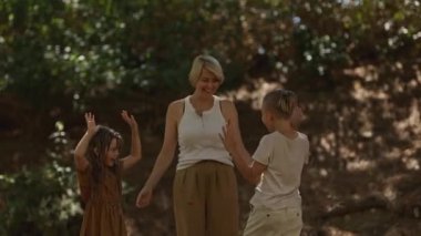 Anne çocuklarıyla oynuyor. Ormana kuru yapraklar atıyor.