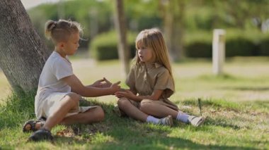 İki küçük çocuk, bir oğlan ve bir kız, güneşli bir parkta ağacın altında birlikte pasta oynuyorlar.