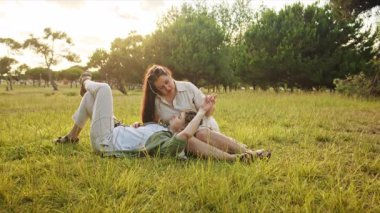 Genç çift çimenlerin üzerinde uzanıp günbatımında doğada romantik bir anın tadını çıkarıyor.