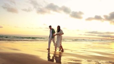 Romantik çift güzel bir gün batımında sahilde yürüyüp koşuyor.