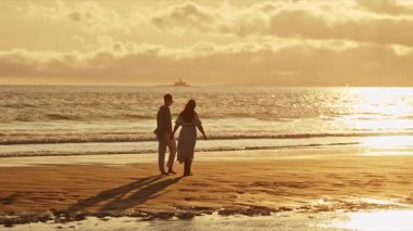 Çiftler gün batımında sahilde romantik yürüyüşler yaparlar.
