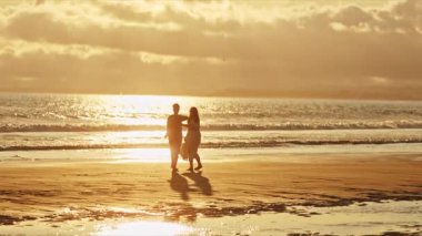 Çiftler, altın bir günbatımında kumsalda romantik bir dans etmekten hoşlanırlar.