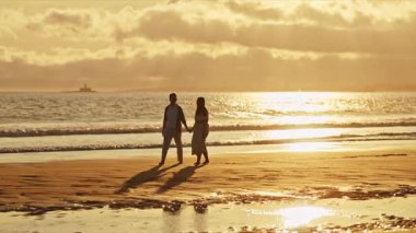 Güzel altın bir günbatımında kumsalda romantik bir yürüyüş yapan genç çift.