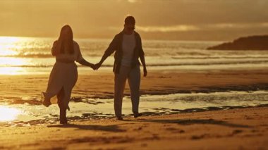 Çiftler, altın saat günbatımında sahilde romantik yürüyüşler yaparlar.