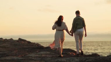 Çift gün batımında deniz kenarında romantik bir yürüyüş yapıyor.