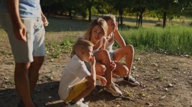 Aile dışarıda oynuyor, yerde çömelmiş, sonra ayağa kalkıyor. Parkta güneşli bir gün, doğa ve temiz havayla neşeli anları yakalıyor.
