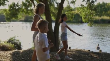 Güneşli bir günde göl kenarında ördek ve kaz besleyen bir grup çocuk.