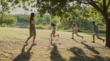 Aile güneşli bir günde parkta kovalamaca oynuyor.