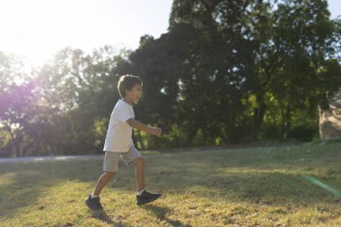 Kaygısız çocuk güneşli bir günün tadını çıkarıyor, parkta koşuyor, çocukluk sevinci ve özgürlüğünü somutlaştırıyor.