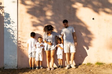 Aile birlikte eğleniyor, güneşli bir günde duvara karşı poz veriyor.