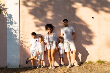 Pembe bir duvara karşı birlikte poz veren mutlu çoklu etnik aile, açık havada kaliteli zaman geçirmenin tadını çıkarıyor.