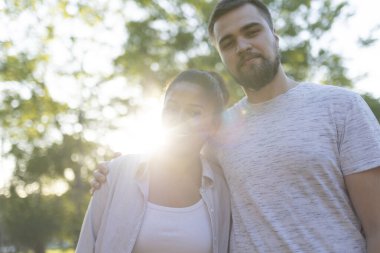 Romantik çift doğada güneşli bir günün tadını çıkarıyor, ağaçların gölgesinde sarılıyorlar.