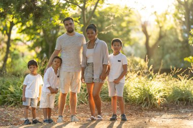 Parkta birlikte poz veren gülümseyen aile güneşli bir günde kaliteli zaman geçiriyorlar.
