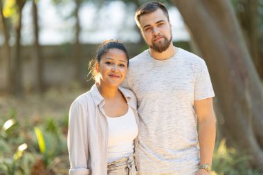 Genç, çok ırklı bir çift parkta gülümsüyor ve birlikte poz veriyorlar.