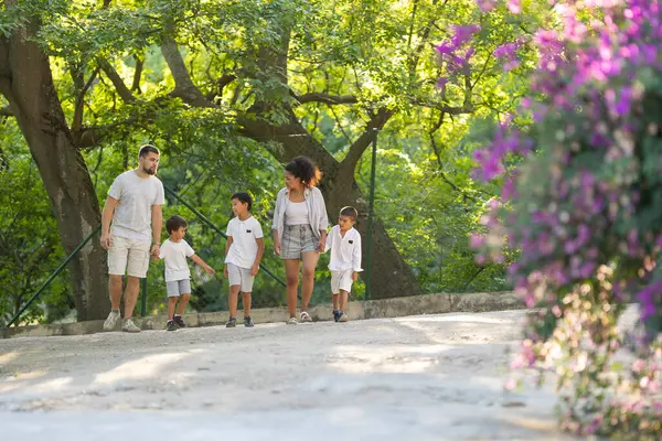 Güneşli bir günde parkta yürüyüş yapan üç çocuklu bir aile.