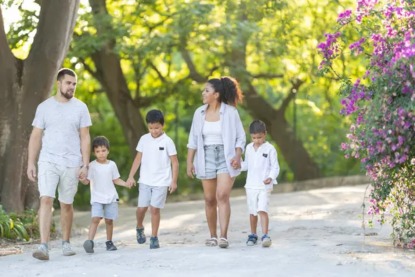 Mutlu bir aile yaz günü parkta yürümekten zevk alıyor, el ele tutuşuyorlar ve kalıcı anılar yaratıyorlar.