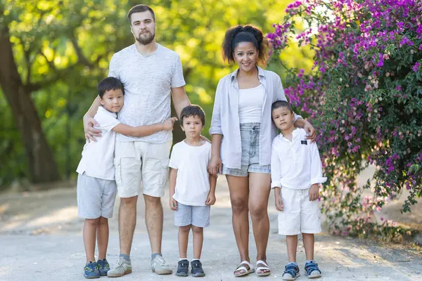 Ebeveynler ve üç çocuk parkta birlikte poz veriyorlar.