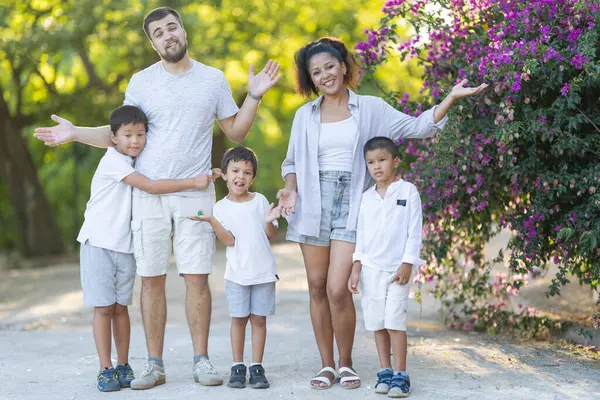 Parkta birlikte poz veren, gülümseyen ve elleriyle hareket eden üç çocuklu bir aile.