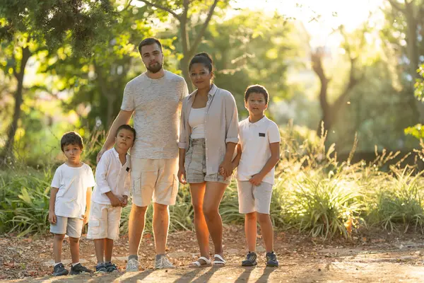 Parkta birlikte poz veren gülümseyen aile güneşli bir günde kaliteli zaman geçiriyorlar.