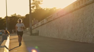 Kararlı sporcu kadın gün batımında taş duvar boyunca koşuyor, egzersizin tadını çıkarıyor.